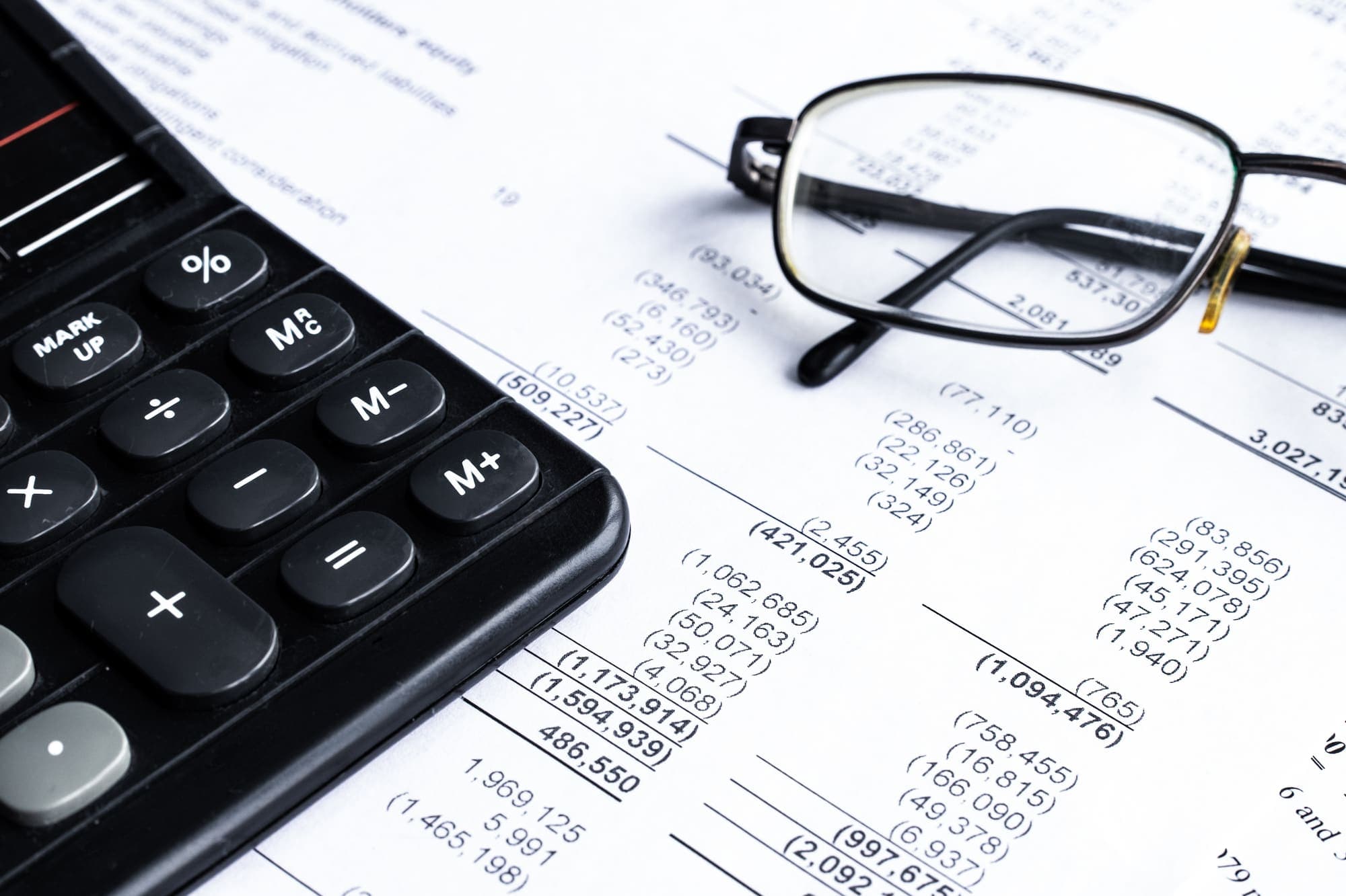 A calculator and reading glasses resting on a printed set of accounts