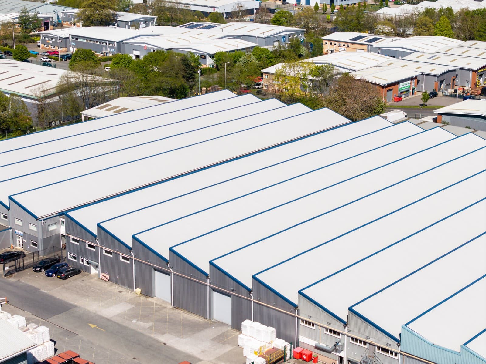 An aerial view of a business park, with rows of large grey industrial units, loading bays and parked cars.