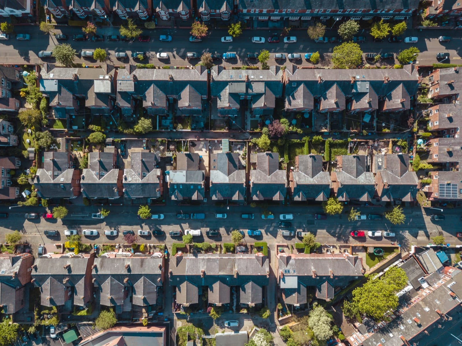 An aerial view looking straight down on rows of terraced houses, with back gardens between them and cars parked along the streets.