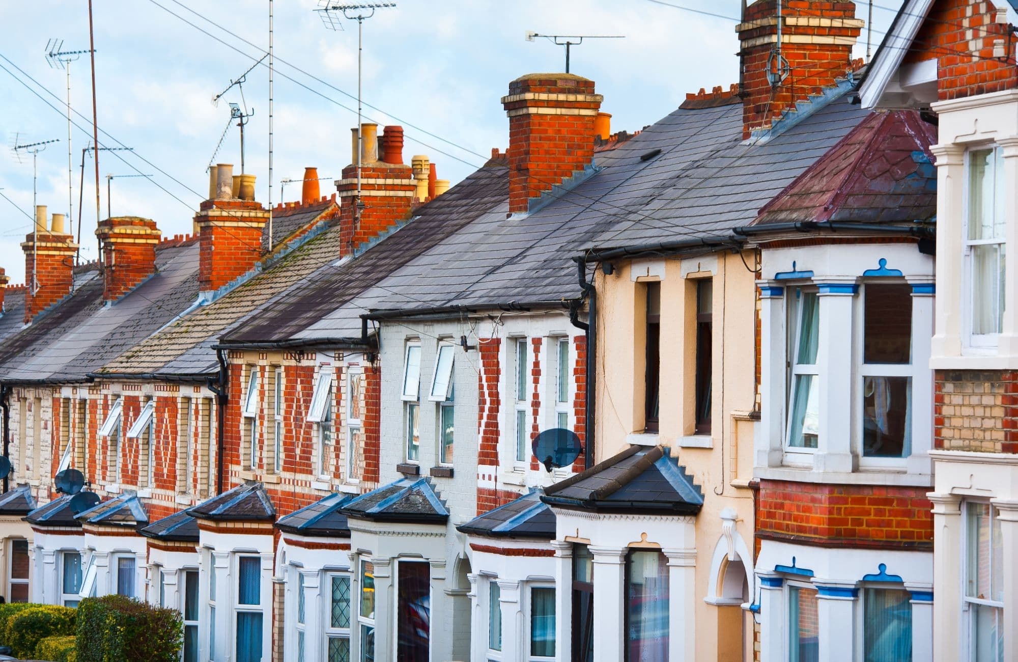 A row of Victorian red brick terraced houses with tall chimneys, slate roofs and white bay windows.
