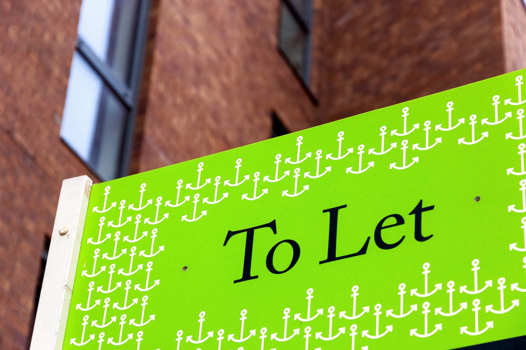 A green To Let board outside a red brick building